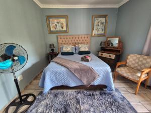 a bedroom with a bed and a fan and a chair at Midvaal Guesthouse in Meyerton