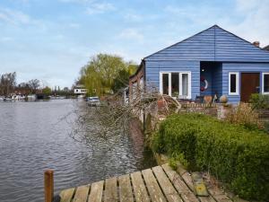 a blue house sitting on the water next to a lake at Riverside Retreat in Beccles