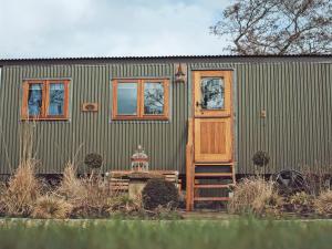 a green house with a wooden door and a ladder at Bailey Huts in Litton