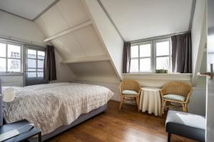 a bedroom with a bed and two chairs and windows at t Huysje van Klippel in Tholen