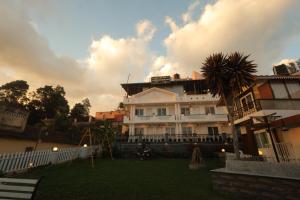 a large white building with a palm tree in a yard at Drizzle Drop Inn in Ooty