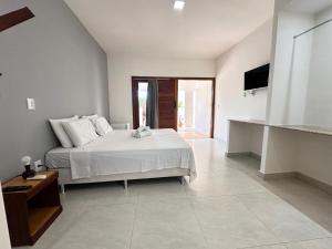 a white bedroom with a bed and a television at 4 Ventos House in São Miguel do Gostoso