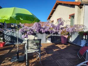 a patio with a table and a green umbrella and purple flowers at PARIS de FLORE Flore in Malakoff
