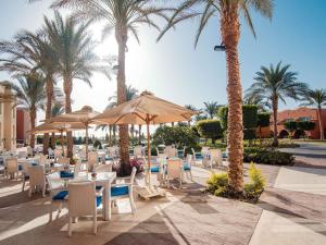a restaurant with chairs and umbrellas and palm trees at Novotel Marsa Alam Beach Resort in Quseir