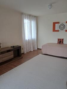 a white bedroom with a bed and a dresser and a window at Apartamento em Pelotas Centro in Pelotas