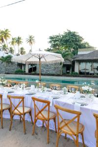 a table with white tables and chairs and an umbrella at Kuarasy Pousada de Charme Japaratinga in Japaratinga