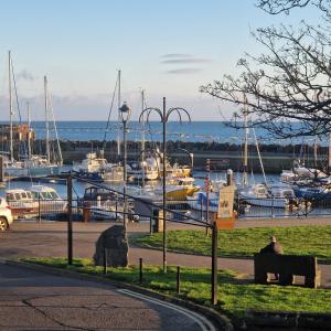 a man sitting on a bench in front of a marina at Beach View Ballycastle Escape in Ballycastle