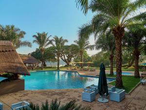 a swimming pool with chairs and an umbrella and palm trees at Pullman Lubumbashi Grand Karavia. in Lubumbashi