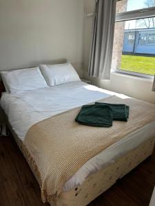 a bed with a green towel on it next to a window at Seabreeze Number 74 includes swimming passes and club entry in Scratby