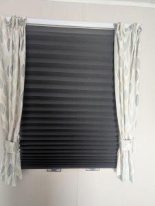 a black horizontal blind in a window with curtains at LuKa25 GC080 in Saint Osyth
