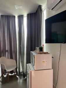 a room with a tv and a refrigerator and a chair at Studio compacto em Camboriú in Camboriú