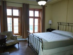 a bedroom with a bed and a chair and windows at L'intendant in Quebec City