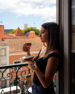 Eine Frau hält einen Teller mit Essen und schaut aus dem Fenster. in der Unterkunft Famous Crows Lisbon Suites in Lissabon