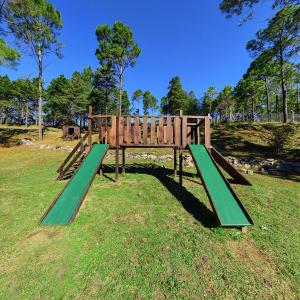 een houten speeltuin met groene glijbanen in het gras bij Pinar del Arroyito in Villa General Belgrano