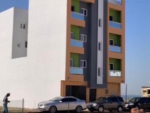 a man standing next to a building with parked cars at Zac Mbao appartement en face de la place in Mbaw
