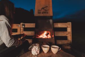 a woman sitting at a table next to a fireplace at Te Awa Glamping in Taumarunui +15 photos