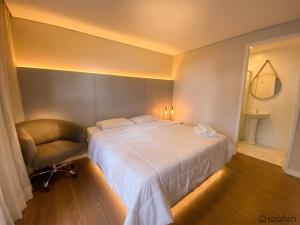 a bedroom with a large white bed and a chair at Wafeh Pampulha Suítes in Belo Horizonte