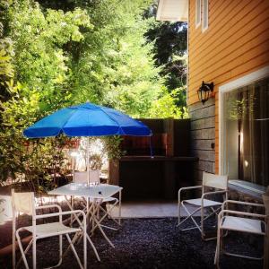 un patio con mesa, sillas y sombrilla azul en Ayelen Cabañas, en Villa La Angostura
