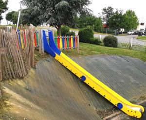 a yellow and blue slide in front of a fence at Brit Hotel Au Pays De Vitré in Étrelles