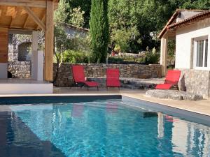 a swimming pool with red chairs and a house at Le Mazet, studio climatisé avec accès piscine in Saint Alban Auriolles