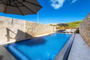 a swimming pool with an umbrella next to a stone wall at Solaris Holiday Home in Għasri