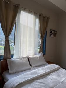 a bed with white sheets and pillows in front of a window at E-RE House, Dirang in Dirang Dzong