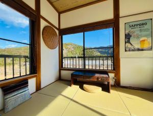 a room with a table and windows with a view at 一棟貸し宿Kanata Riverview House in Kawanehon