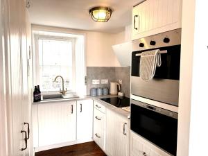 a kitchen with white cabinets and a sink and a stove at Para Handy Cottage, Inveraray in Inveraray