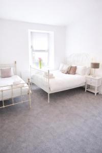 a white bedroom with two beds and a window at Coquet Nest AMBLE in Amble