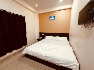 a bedroom with a bed with white sheets and a television at Hotel Sundaram in Deoghar