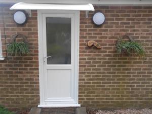 a white door on a brick wall with two plants at Acorns in Wavehorne