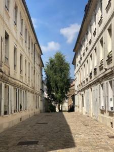 an empty street with two buildings and a tree at La Petite Paroisse Classé 3 étoiles Elégant & Proche Marché in Versailles