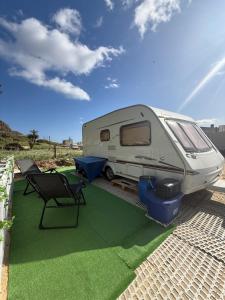 a white caravan parked on a lawn with a chair at Little hideaway in Costa da Caparica