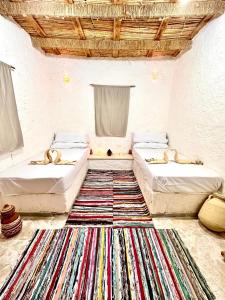 two beds in a room with a rug at Adrartaziry in Siwa