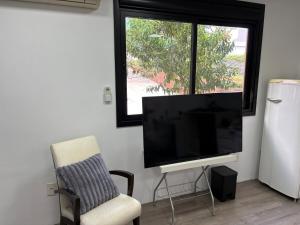 a living room with a flat screen tv and a chair at Estúdio com suíte super confortável no centro in Ijuí