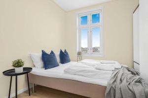 a white bed with blue pillows and a window at Contemporary city-apartement with views of the dock! in Bergen
