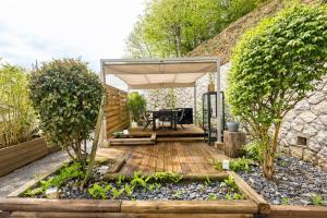 a garden with a wooden deck with a table under a canopy at Acmé Appartement 200 m du lac d'Annecy in Angon