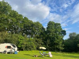 a caravan parked in a field with a table and an umbrella at Camping pod in Greatham