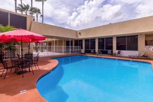 a swimming pool with tables and chairs and an umbrella at Clarion Inn near McAllen Airport in McAllen