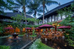 a restaurant with tables and chairs and palm trees at Ramayana Suites and Resort in Kuta