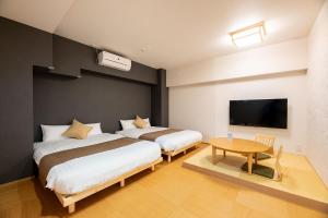 two beds in a room with a table and a tv at YASAKA Hotel in Kagoshima