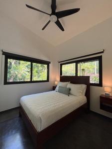 a bedroom with a ceiling fan and two windows at Luxury Riverfront House 3BR BBQ Jungle views & walk to river in Parrita