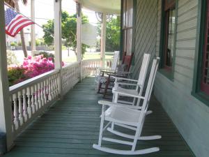 uma fila de cadeiras de baloiço num alpendre com uma bandeira americana. em Pensacola Victorian Bed & Breakfast em Pensacola