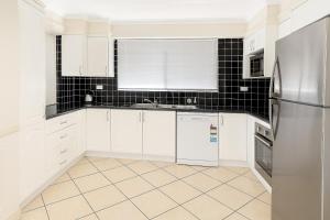 a kitchen with white cabinets and a refrigerator at Redcliffe Villa in Redcliffe +1 photo