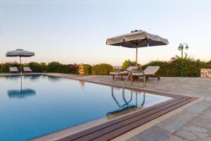 a swimming pool with an umbrella and two chairs and a bench at Belvedere Beachfront Villa in Afantou