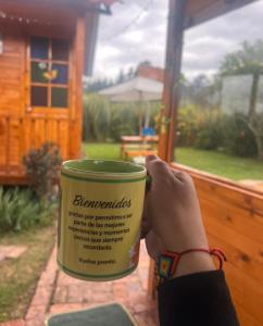 a person holding a coffee cup in front of a house at Cabaña Los Linos in Guasca