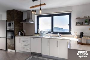 a kitchen with white cabinets and a large window at Casa Maré by PontaNegraAzores in Angra do Heroísmo