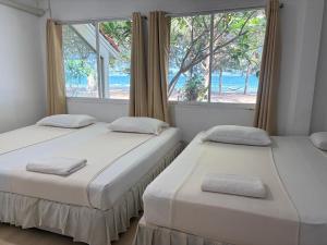 two beds in a room with a window at Tharnvara Resort in Ban Khok Sung