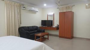 a bedroom with a bed and a chair and a television at Hotel Tamilnadu Trichy in Tiruchirappalli