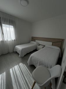 a white room with two beds and a chair at Habitaciones A Postiña in Areas